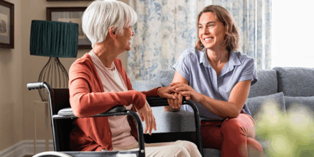 A young woman being supportive and holding hands with an older woman in a wheelchair in hospice care - Three Ways to Support Friends and Family in Hospice Care - Northern Illinois Hospice